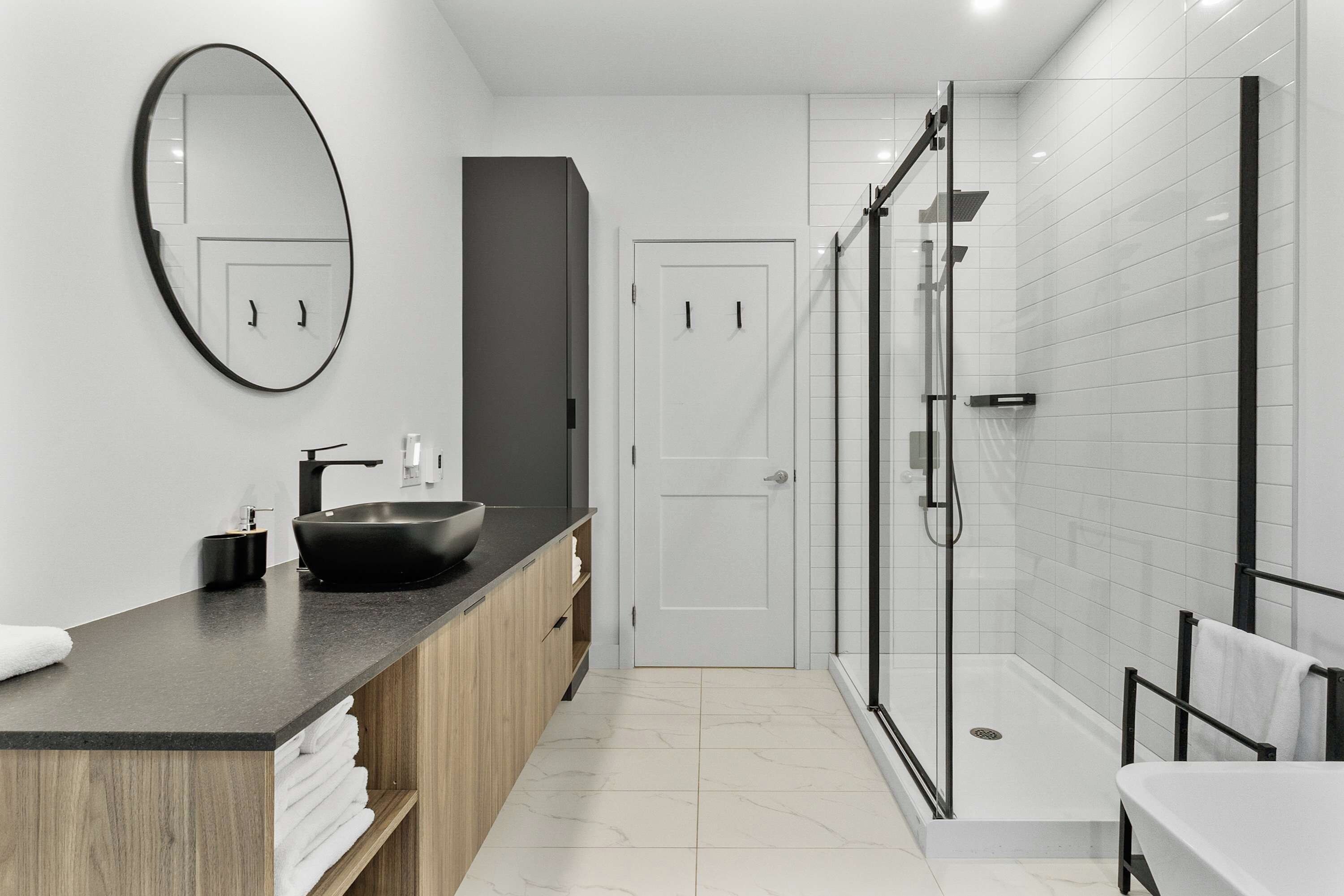 Une salle de bain moderne avec un lavabo sur colonne noir, un grand miroir et une douche à parois de verre.