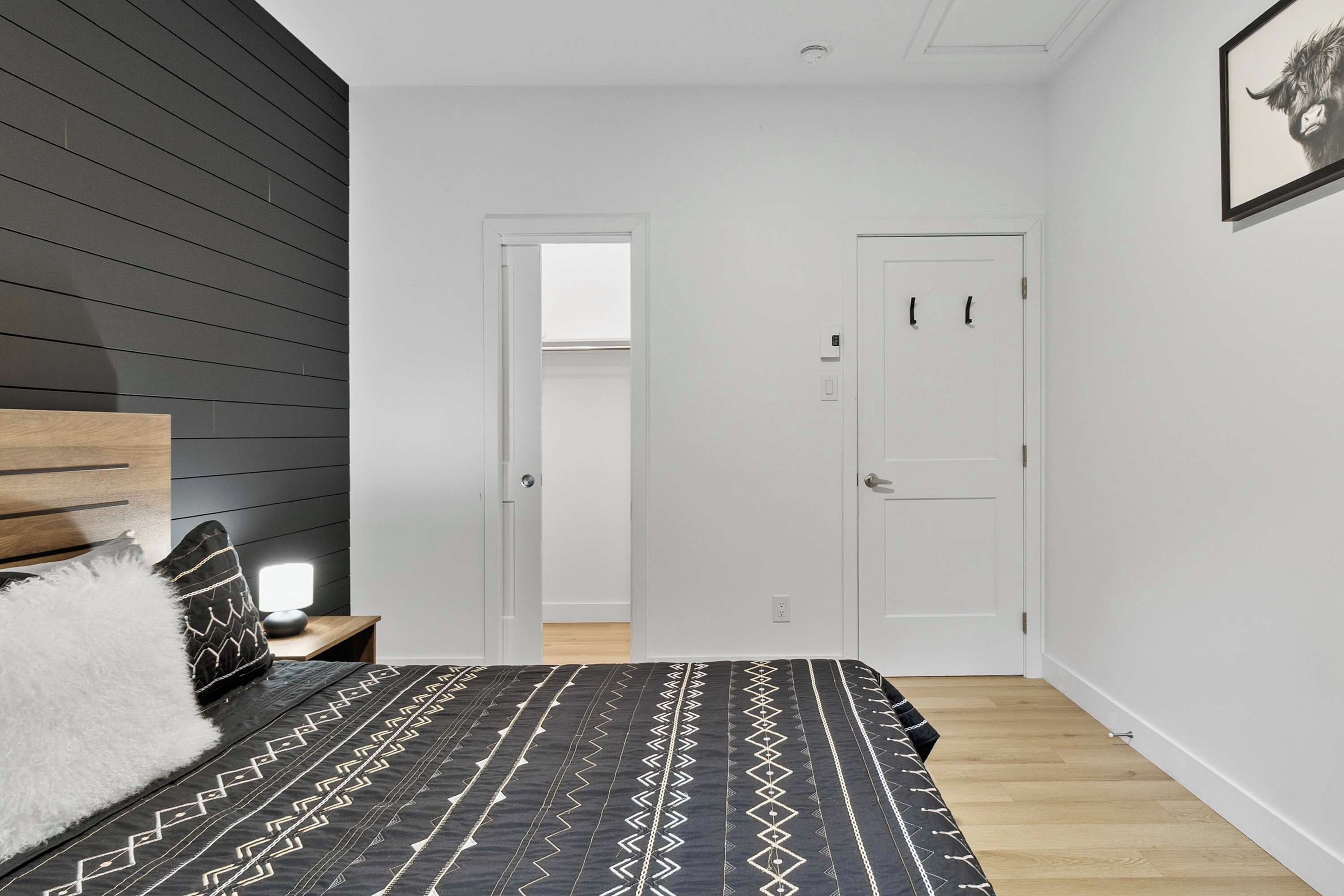 A bedroom with a bed, a nightstand, a wall-mounted shelf, a door, and a framed picture on the wall.