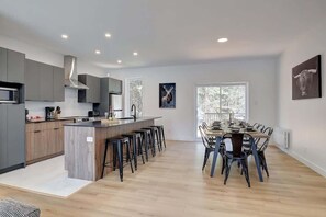 A modern kitchen with a central island, bar stools, and a dining area with chairs.