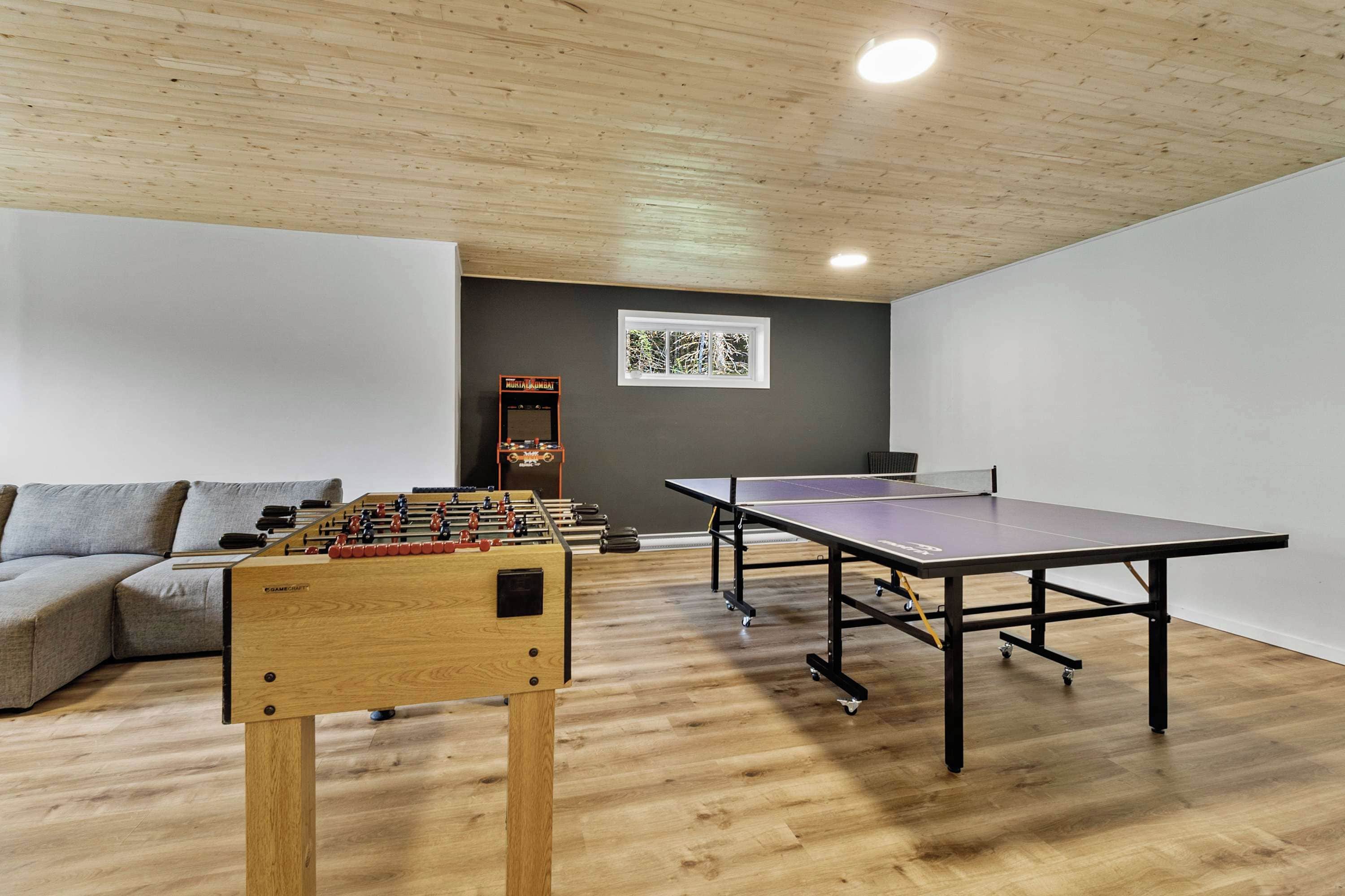 A room with a foosball table, ping pong table, and a sofa.