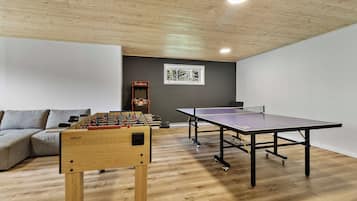 A room with a foosball table, ping pong table, and a sofa.