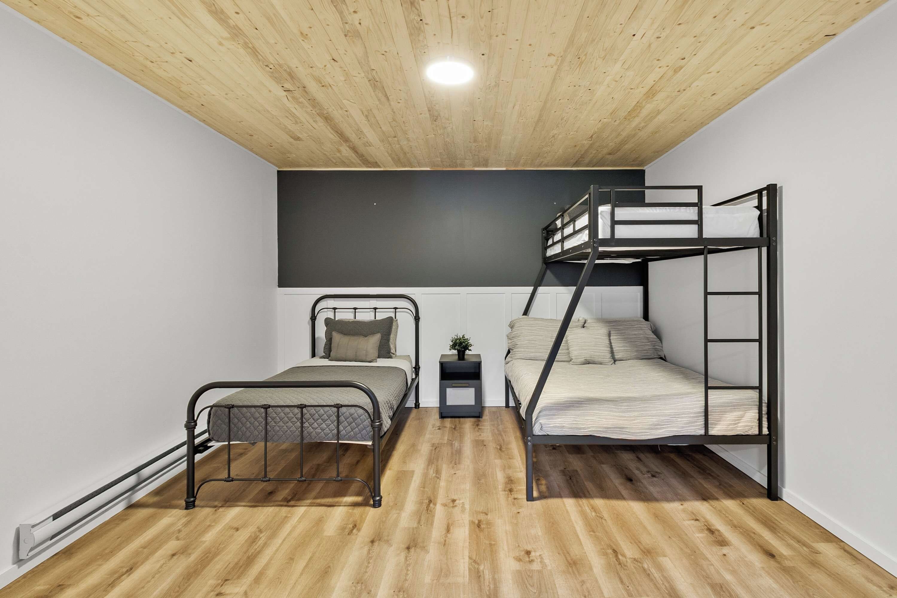 Une chambre avec un lit superposé, un lit simple, une petite table avec une plante et un plancher en bois.