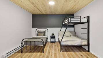 Une chambre avec un lit superposé, un lit simple, une petite table avec une plante et un plancher en bois.