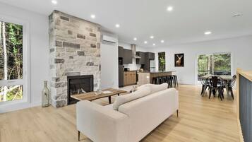 A modern living space with a stone fireplace, a sofa, a dining area, and a kitchen.
