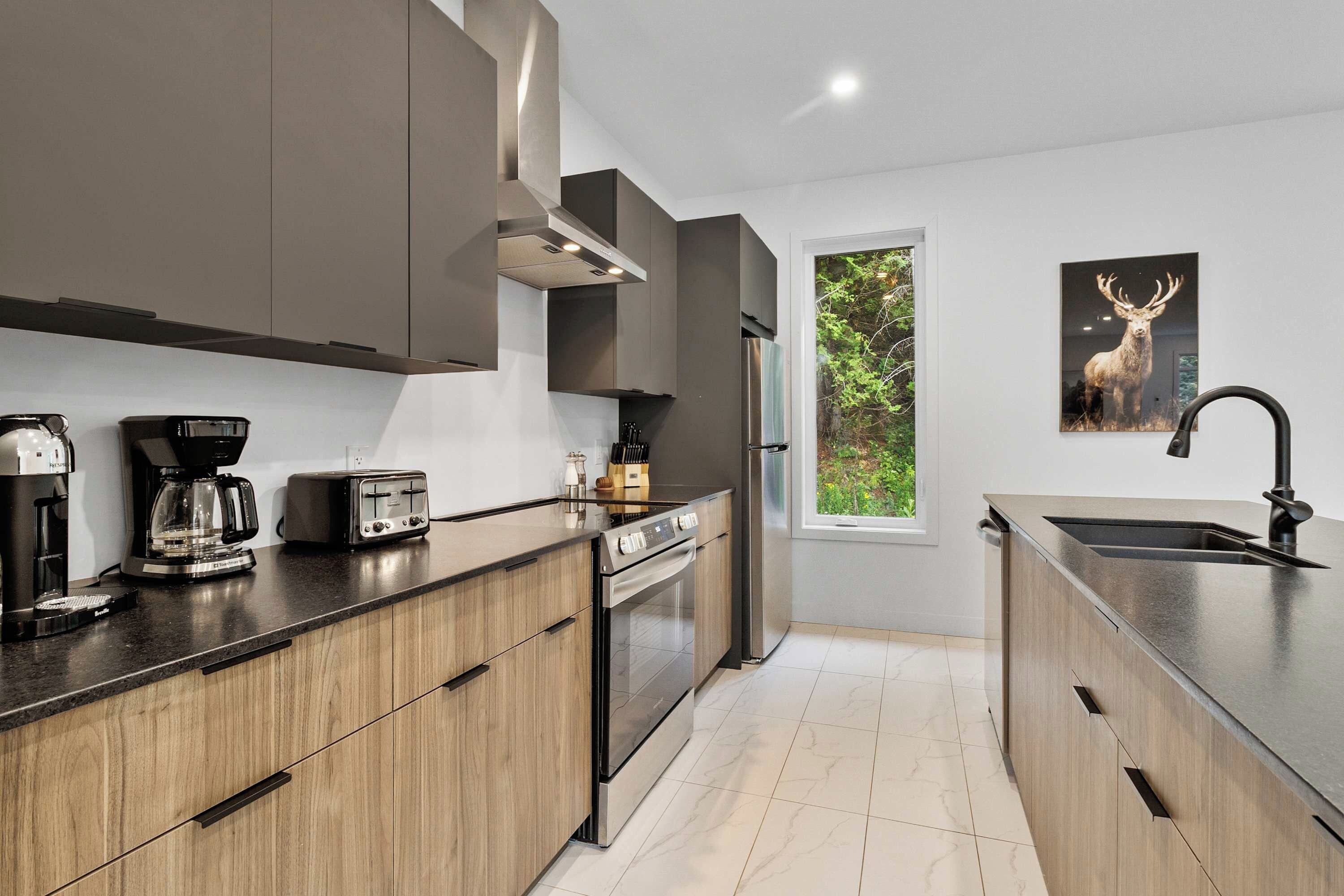 A modern kitchen with wooden cabinets, a stainless steel refrigerator, a coffee maker, a toaster, and a sink.