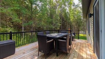 A deck with a table and chairs, surrounded by a black railing, overlooking a wooded area.