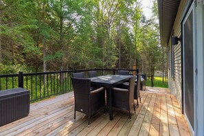 Varanda com mesa e cadeiras, cercada por guarda-corpo preto, com vista para uma área arborizada.