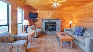 A cozy cabin interior with a stone fireplace, wooden walls, a ceiling fan, and a television mounted on the wall. - Chalet with 2 Bedrooms lakeside to Dale Hollow Lake #17 (Byrdstown)