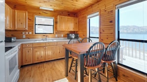 Une cuisine rustique aménagée dans une cabane en bois, avec une table et des chaises, de grandes fenêtres et une vue sur l’extérieur.