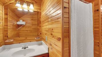 A wooden cabin bathroom with a white sink, mirror, and hanging lights.