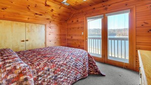 Habitación de cabaña de madera con cama, ventilador de techo y una ventana grande con vista a un cuerpo de agua.