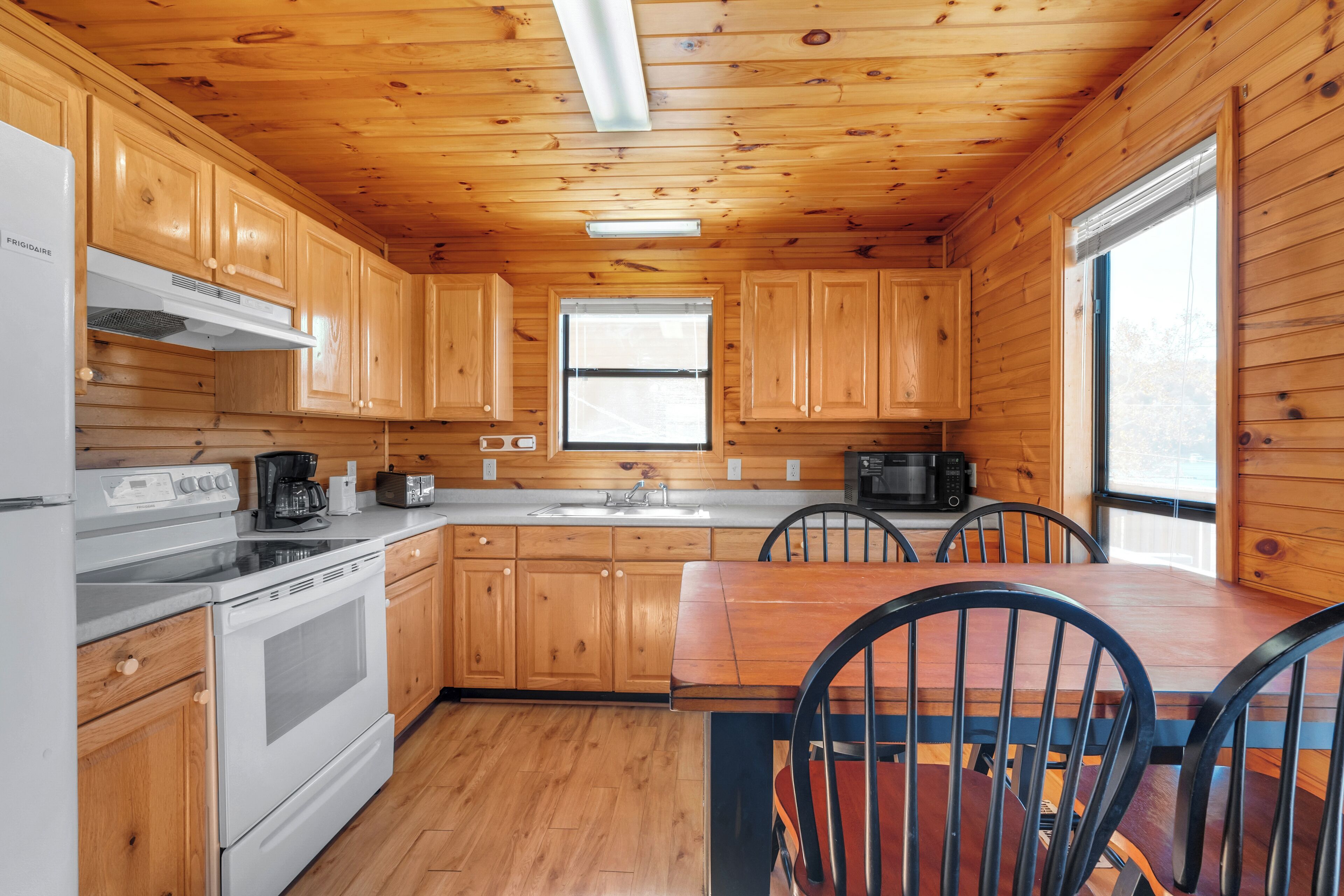 A wooden cabin kitchen with a stove, sink, and dining table.