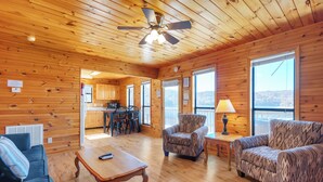 A spacious living area with a wooden ceiling, a dining table, two patterned sofas, and a kitchen in the background.
