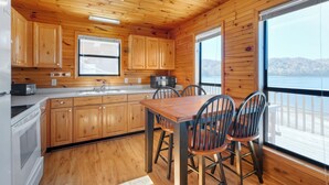 A wooden cabin kitchen with a dining table and chairs, large windows, and a view of the outdoors.