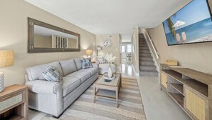 A living room with a sofa, coffee table, and TV. There is a staircase leading to another level. - Tranquil Siesta Key Retreat ~ Walk to Beach ~ Pool (Siesta Key)