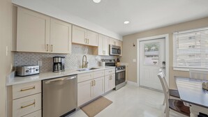 A modern kitchen with beige cabinets, stainless steel appliances, and a dining area with a table and chairs. - Tranquil Siesta Key Retreat ~ Walk to Beach ~ Pool (Siesta Key)