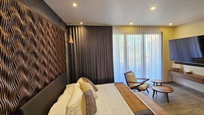 Ein modernes Hotelzimmer mit einem großen Bett, einem an der Wand montierten Fernseher, einer Sitzecke mit einem Sessel und einem kleinen Tisch sowie einer dekorativen Wandverkleidung.
