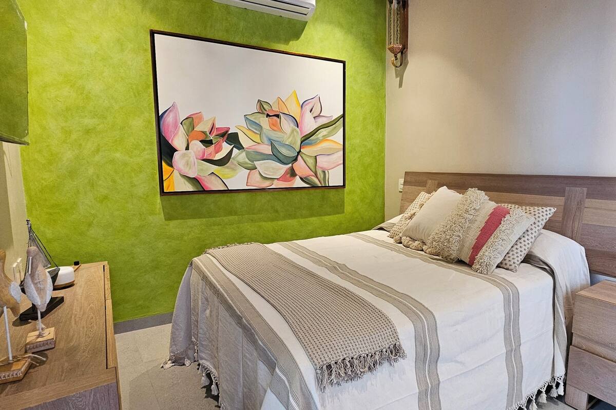 Une chambre à coucher comprenant un lit, une table de chevet, un climatiseur fixé au mur et une sculpture d’oiseau décorative.