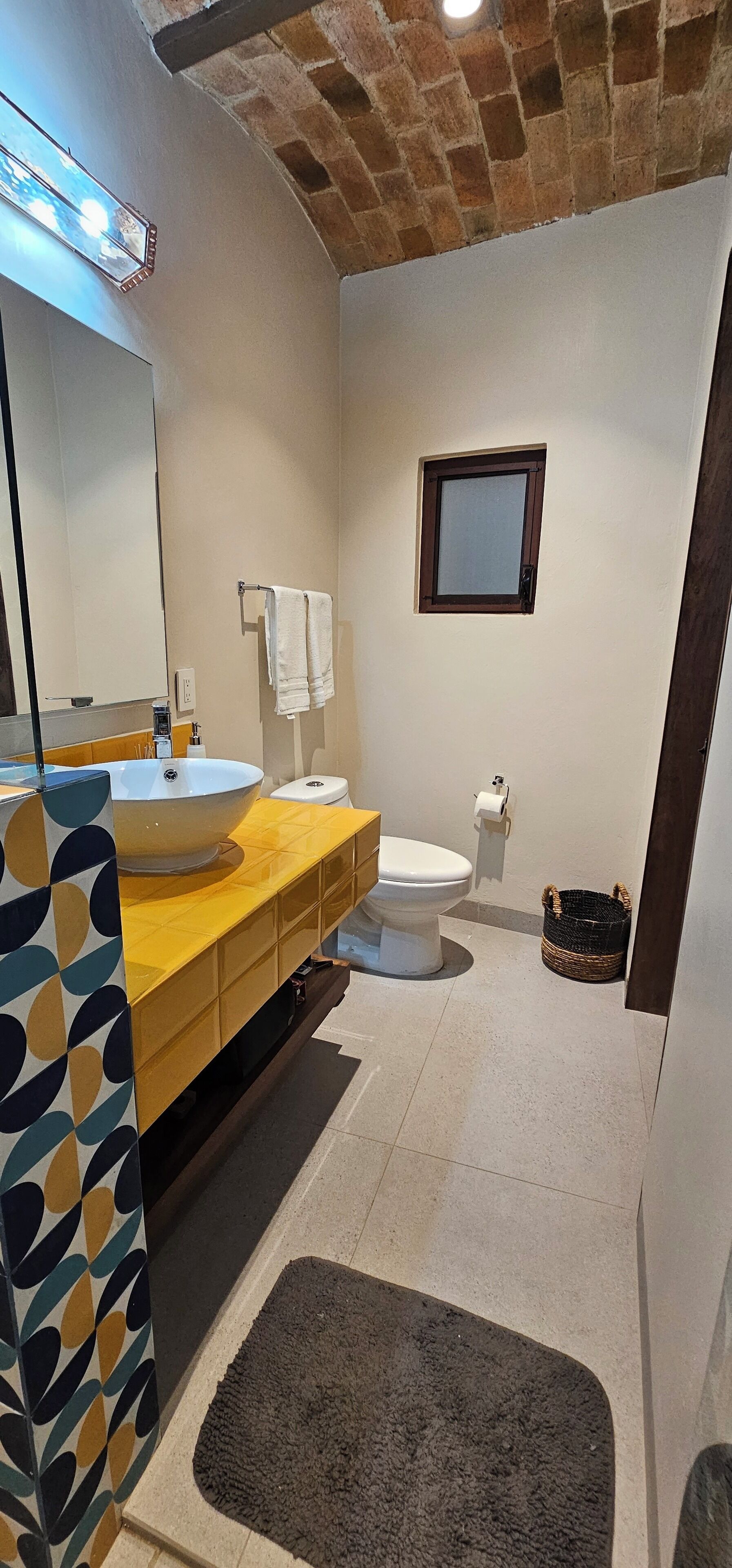 A bathroom with a yellow vanity, a large mirror, a white toilet, and a small window.