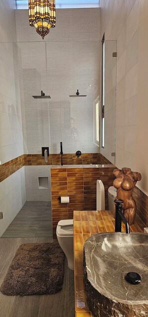Ein modernes Badezimmer mit Waschtisch, großem Spiegel, freistehender Spüle und Duschbereich.