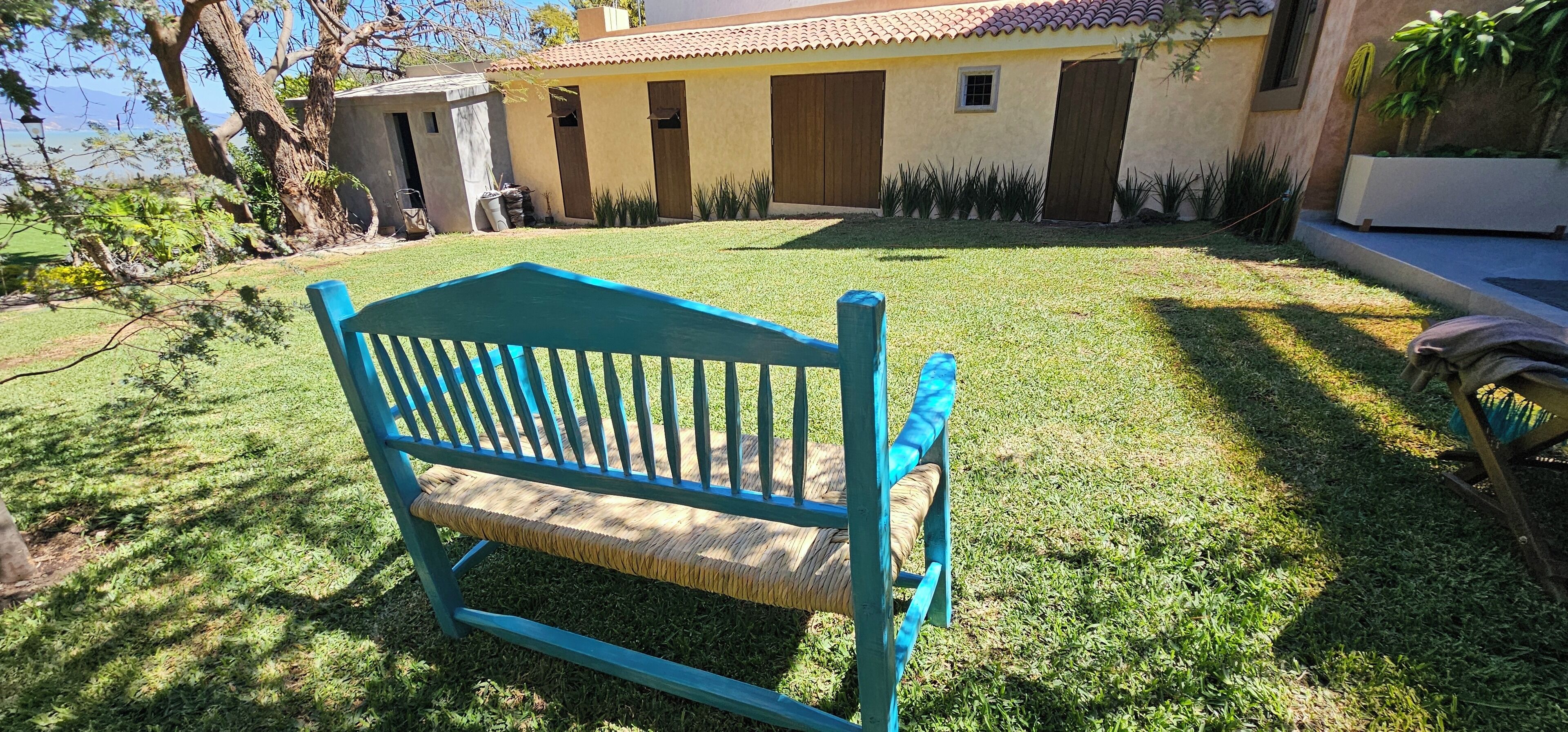 Un banco azul en un jardín con césped, con una casa al fondo.