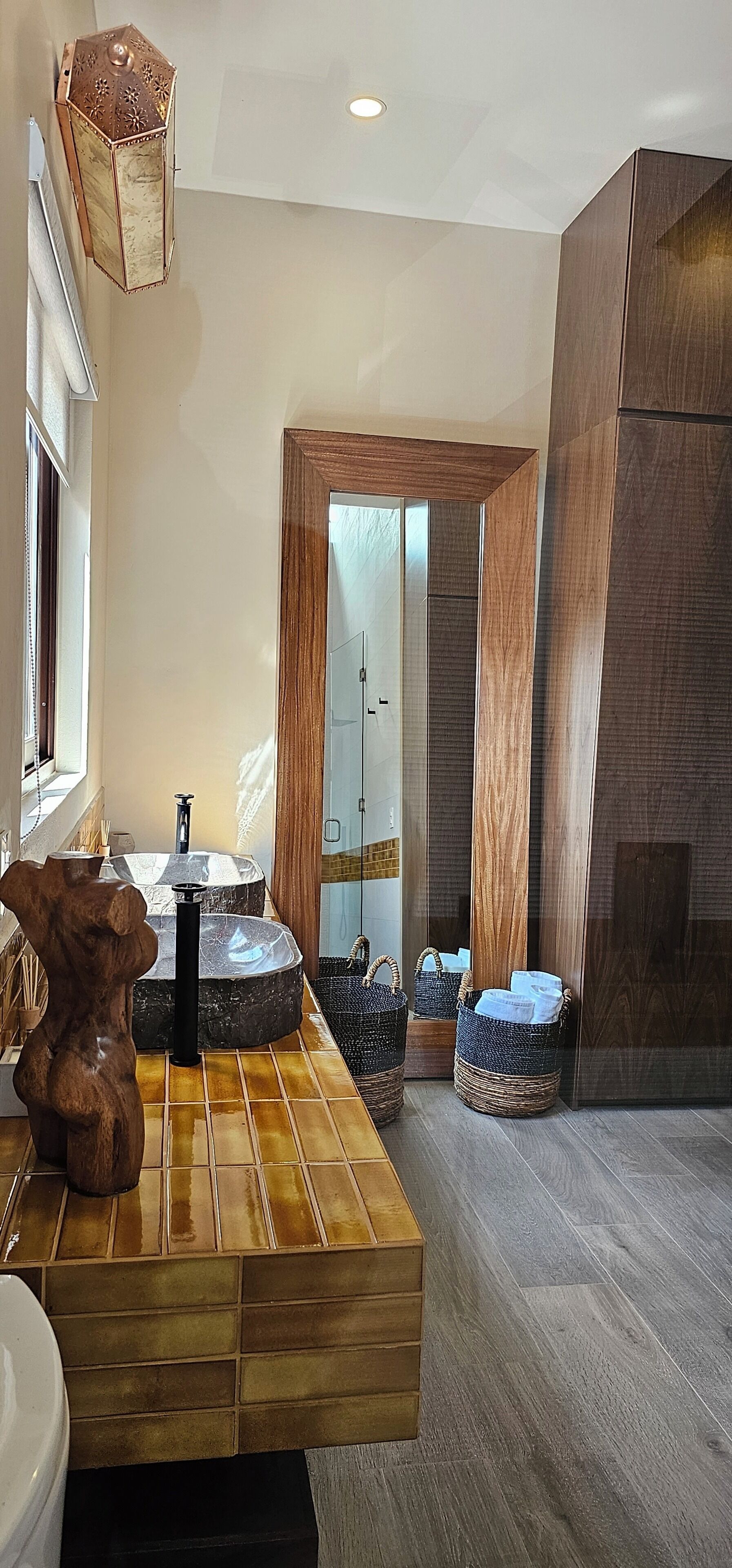 A modern bathroom with a wooden vanity, a marble sink, and a large mirror.