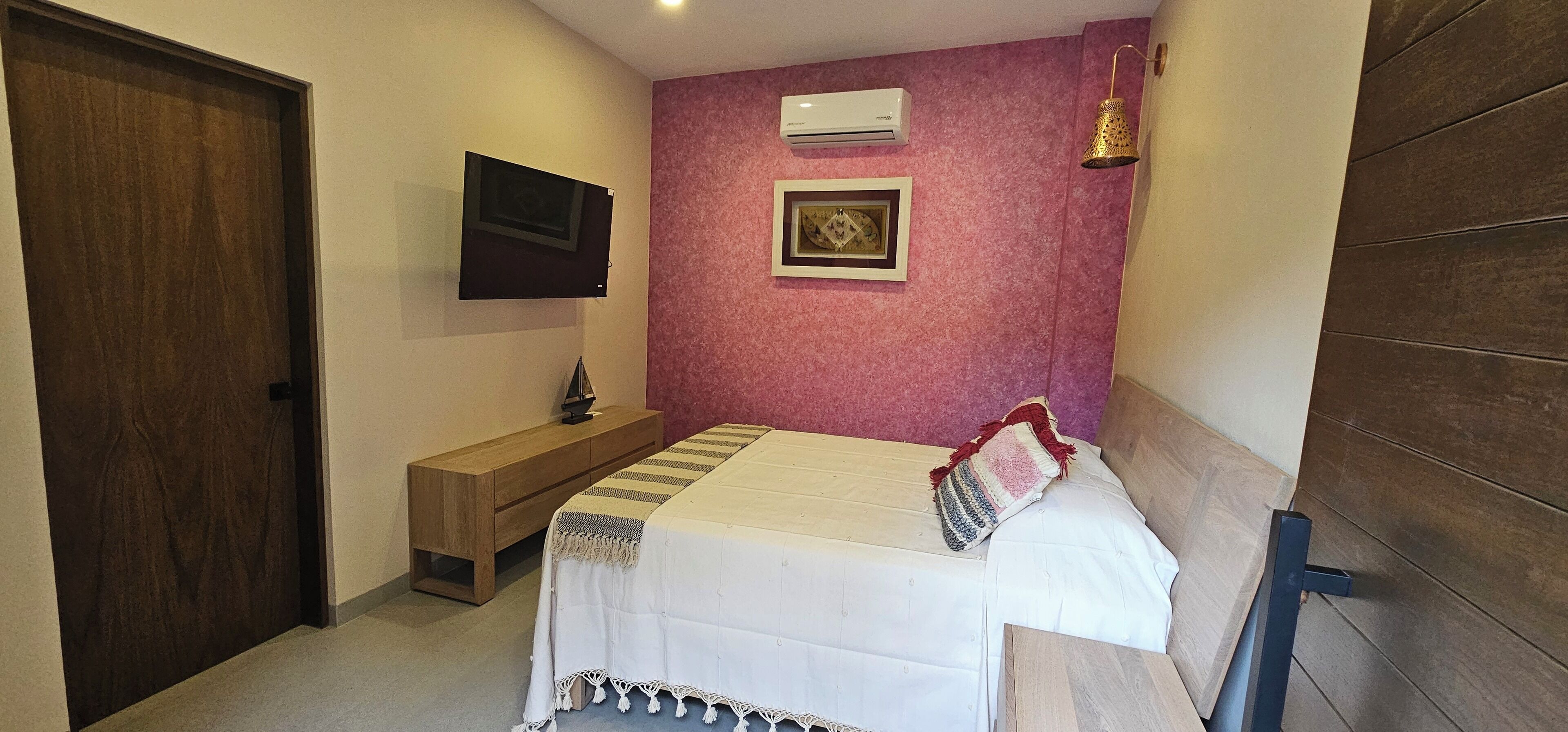 Una camera da letto con un letto, una panca in legno, una TV a muro e un condizionatore d'aria.