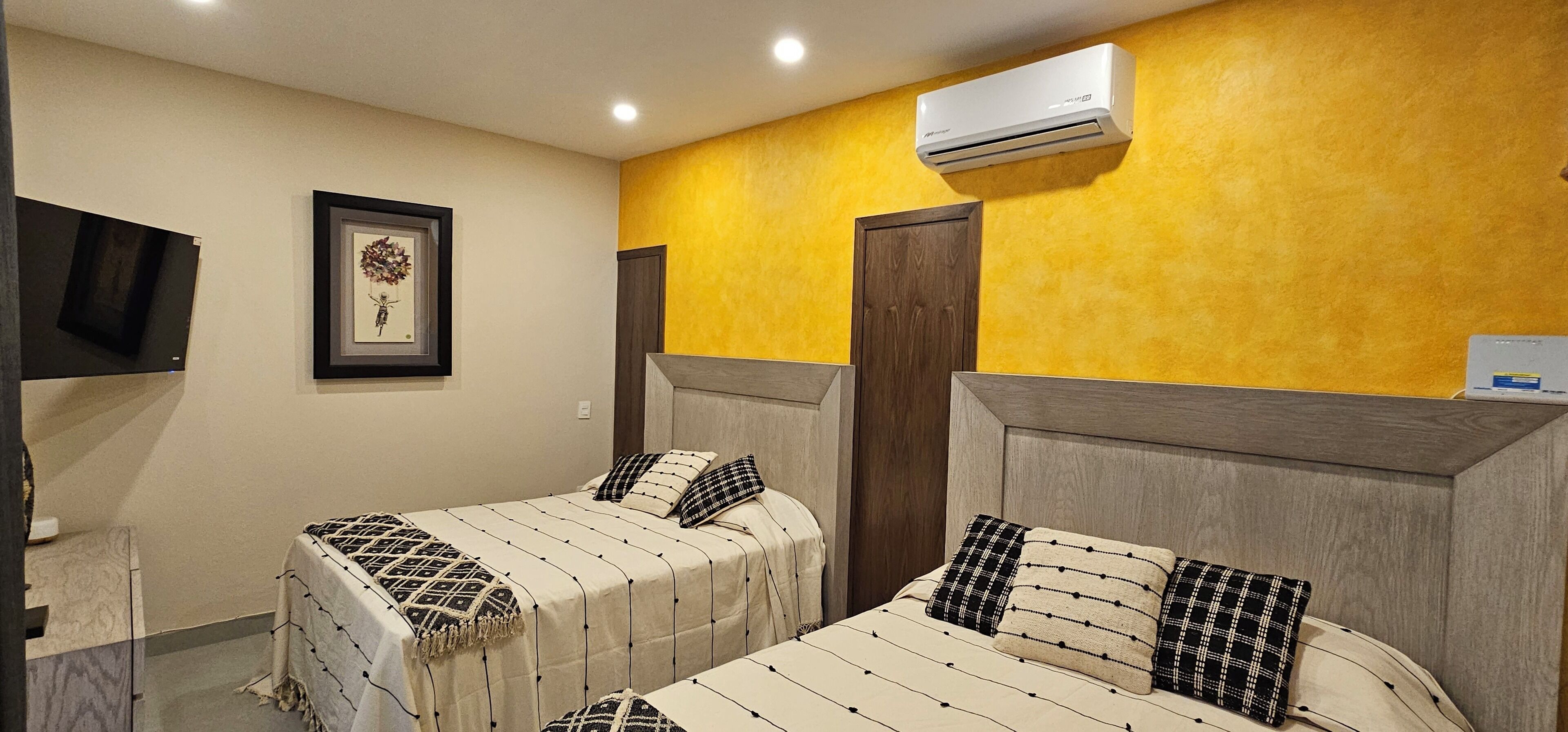 A hotel room with two beds, a TV, a framed picture, and an air conditioner.