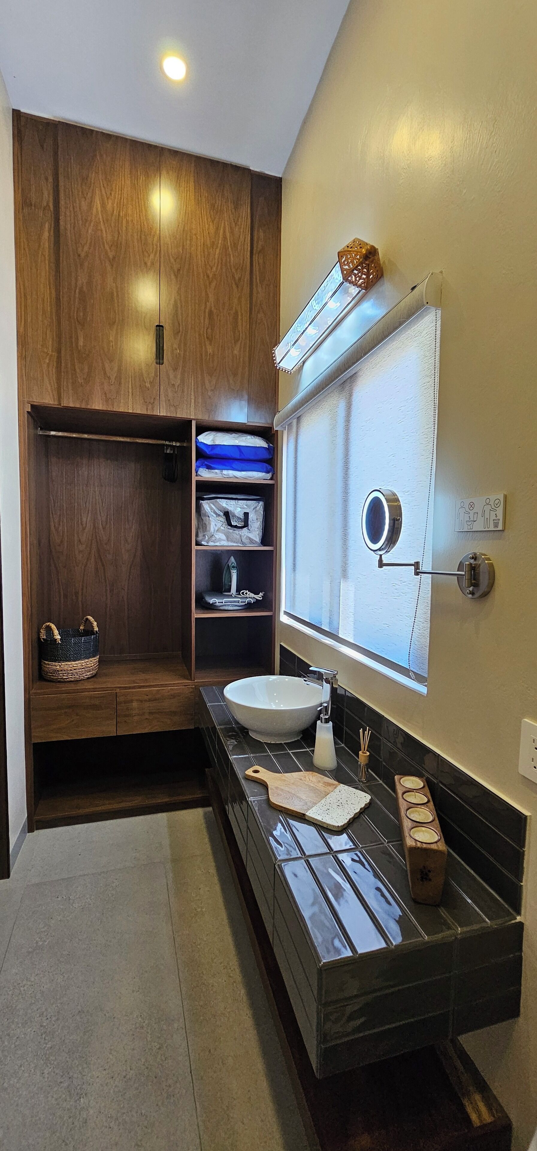 A modern bathroom with a wooden wardrobe, a large mirror, a sink, and a vanity with a cutting board.
