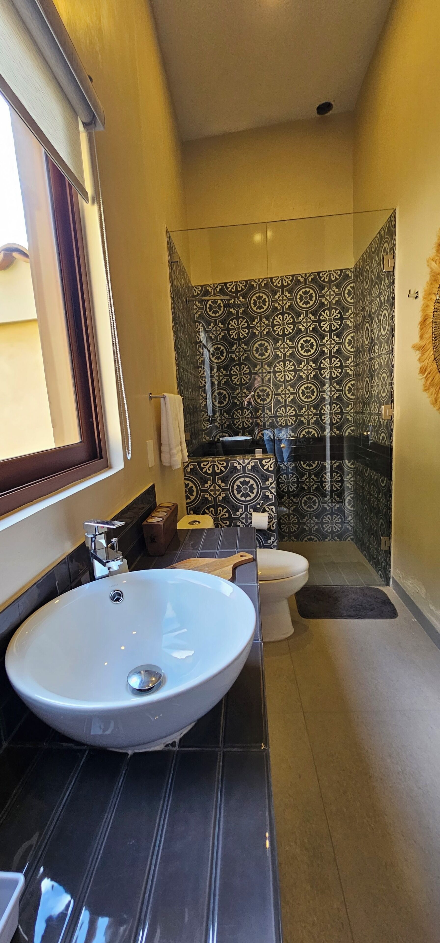 A bathroom with a large white sink, a toilet, and a shower area with patterned tiles.