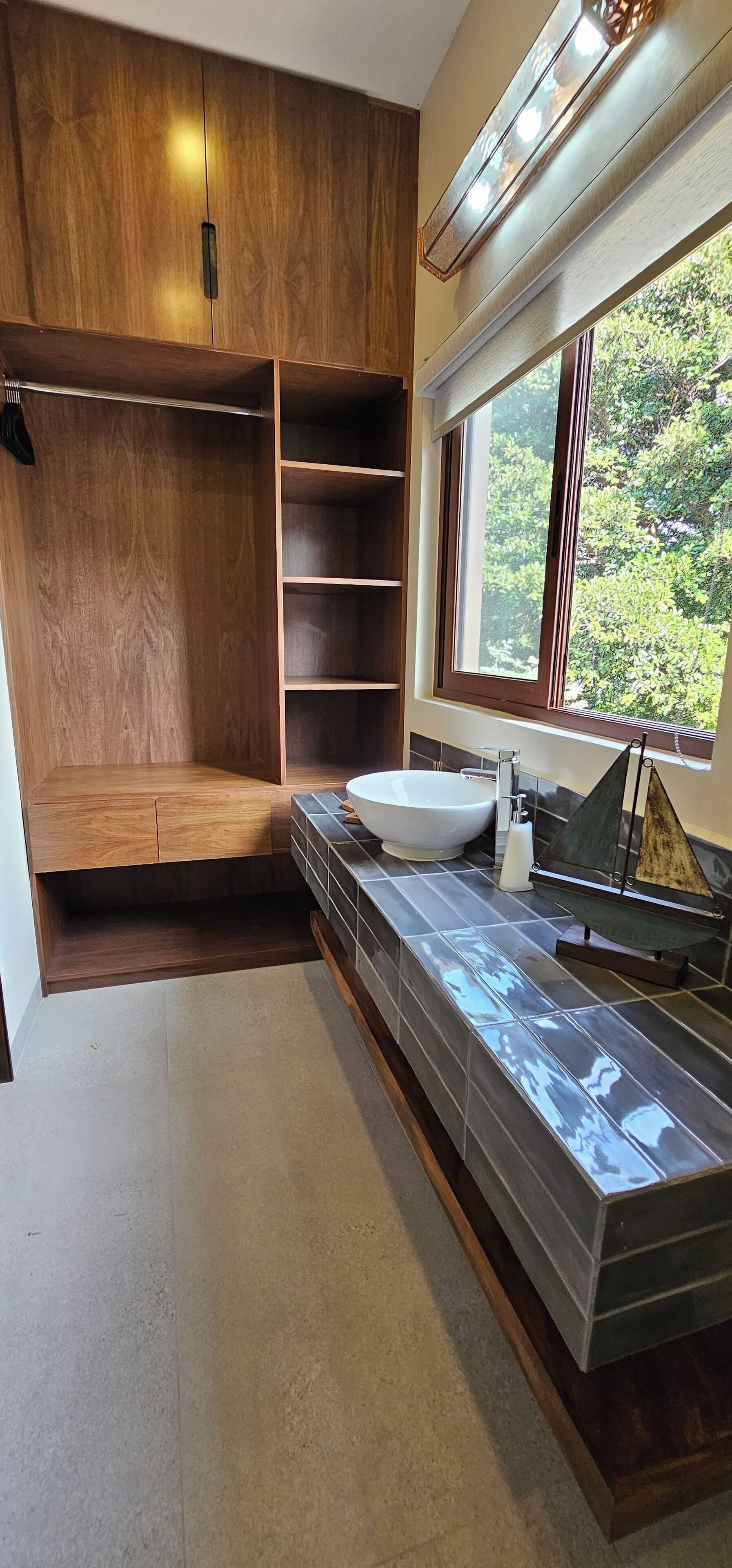 A modern bathroom with a wooden vanity, a large window, and a view of greenery outside.