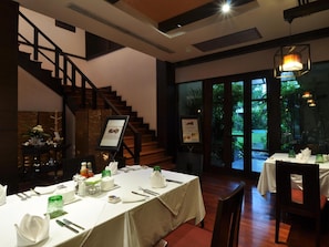 Une salle à manger avec des tables dressées pour le service, un escalier et une vue sur l’extérieur.