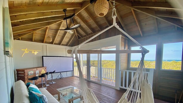 A spacious room with a hammock, a white sofa, a large screen, and a balcony with a view of the sea. - A Spacious Ocean View Villa, steps away from Punta Cocos bioluminescence beach.  (Holbox)