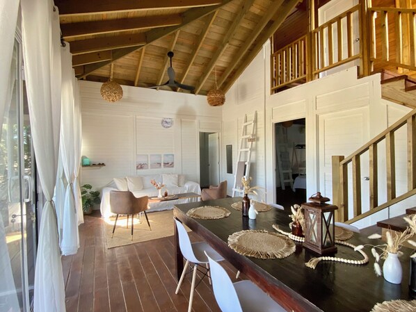 A spacious living area with a wooden ceiling, a dining table set with placemats, and a staircase leading to an upper level. - A Spacious Ocean View Villa, steps away from Punta Cocos bioluminescence beach. (Holbox)