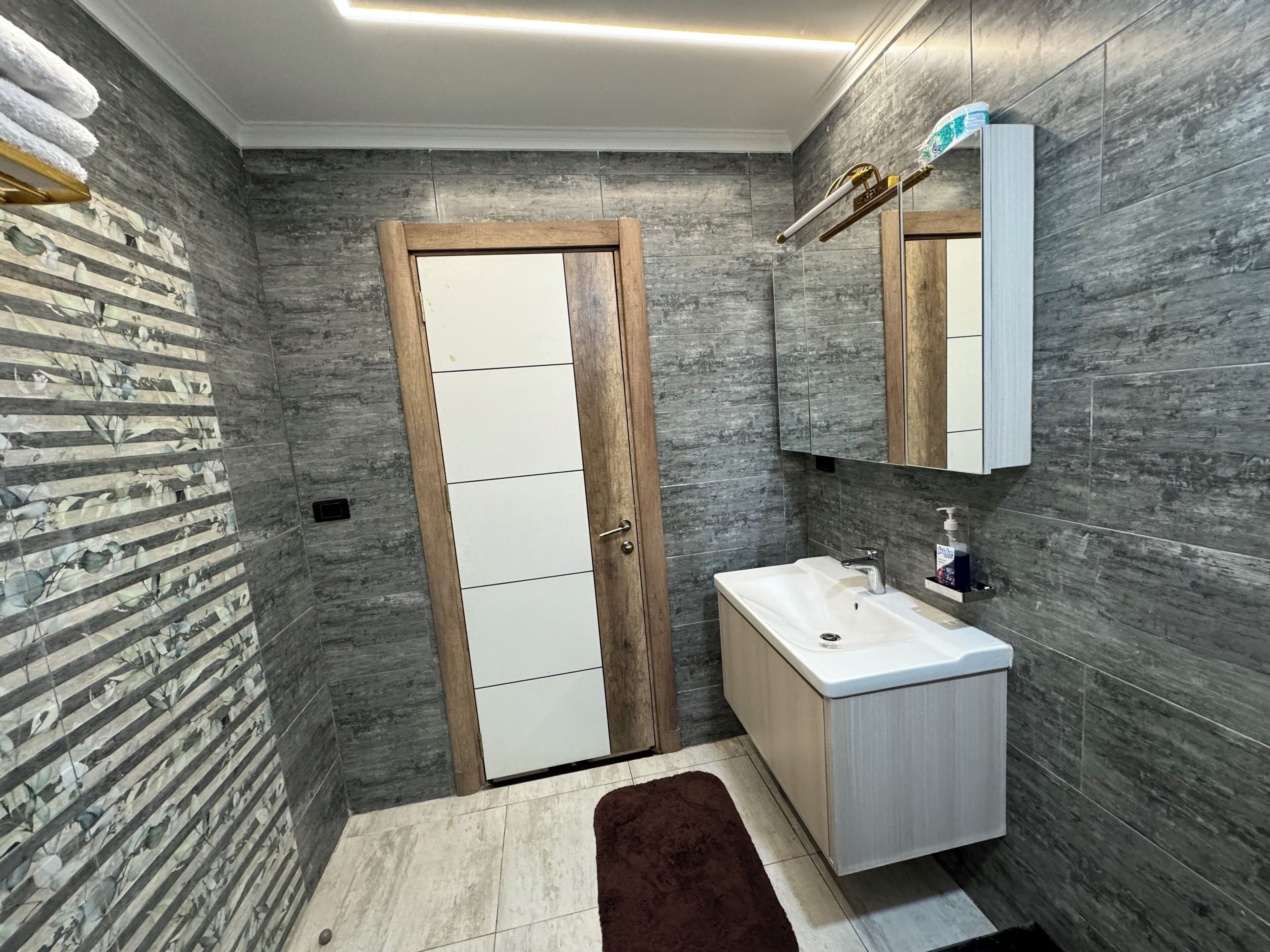 Un baño moderno con puerta de madera, un lavabo blanco y un espejo encima.