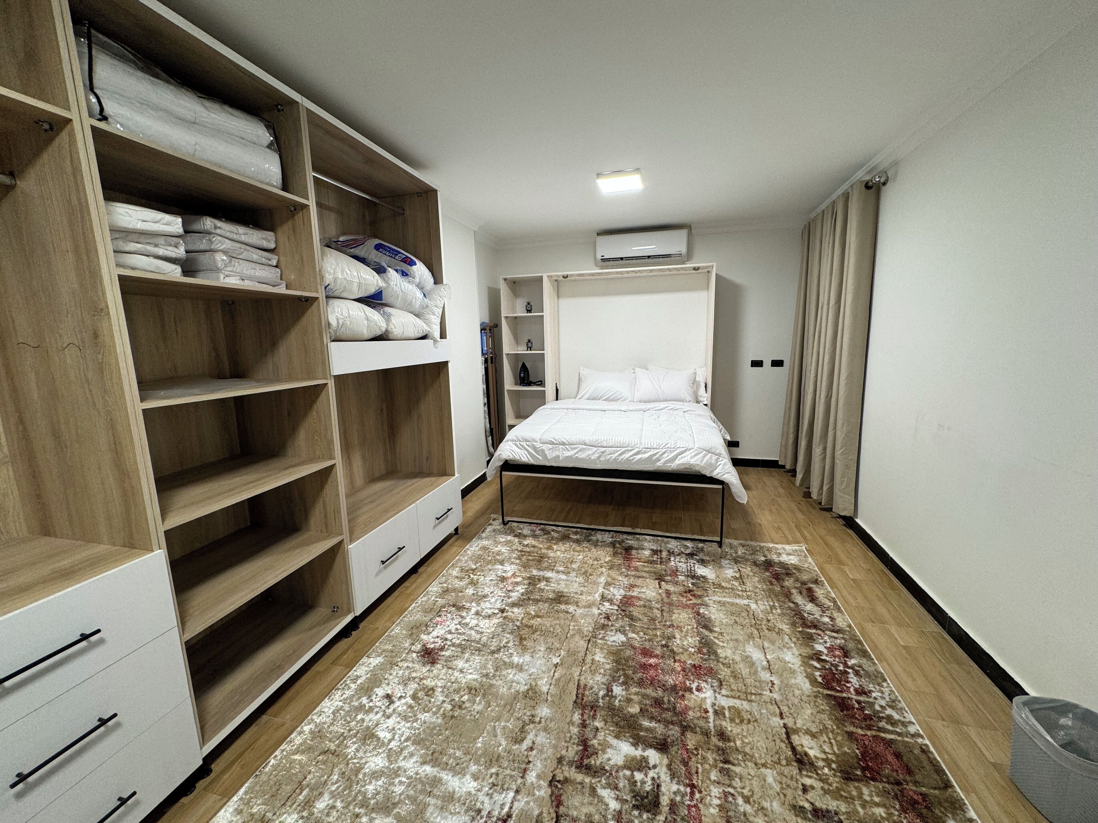 Un dormitorio con cama, armario de madera, estanterías y alfombra.