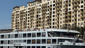 A multi-story hotel with balconies and a boat docked in front. - Relaxation (Aswan)