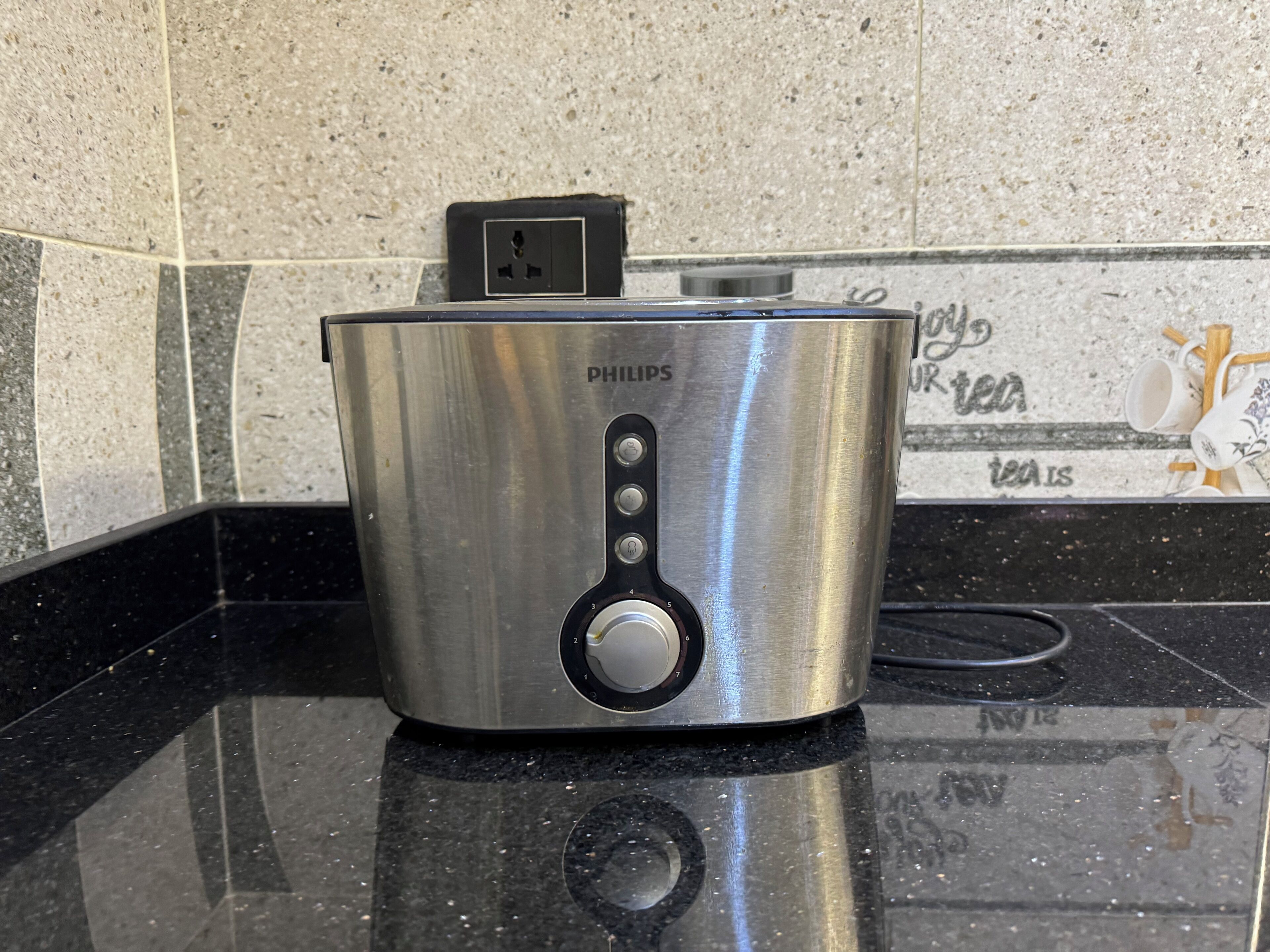 A stainless steel Philips electric kettle on a black countertop with a tiled backsplash.