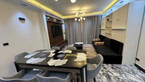 A modern dining area with a marble floor, a black dining table with lace placemats, grey upholstered chairs, and a chandelier. - Relaxation (Aswan)