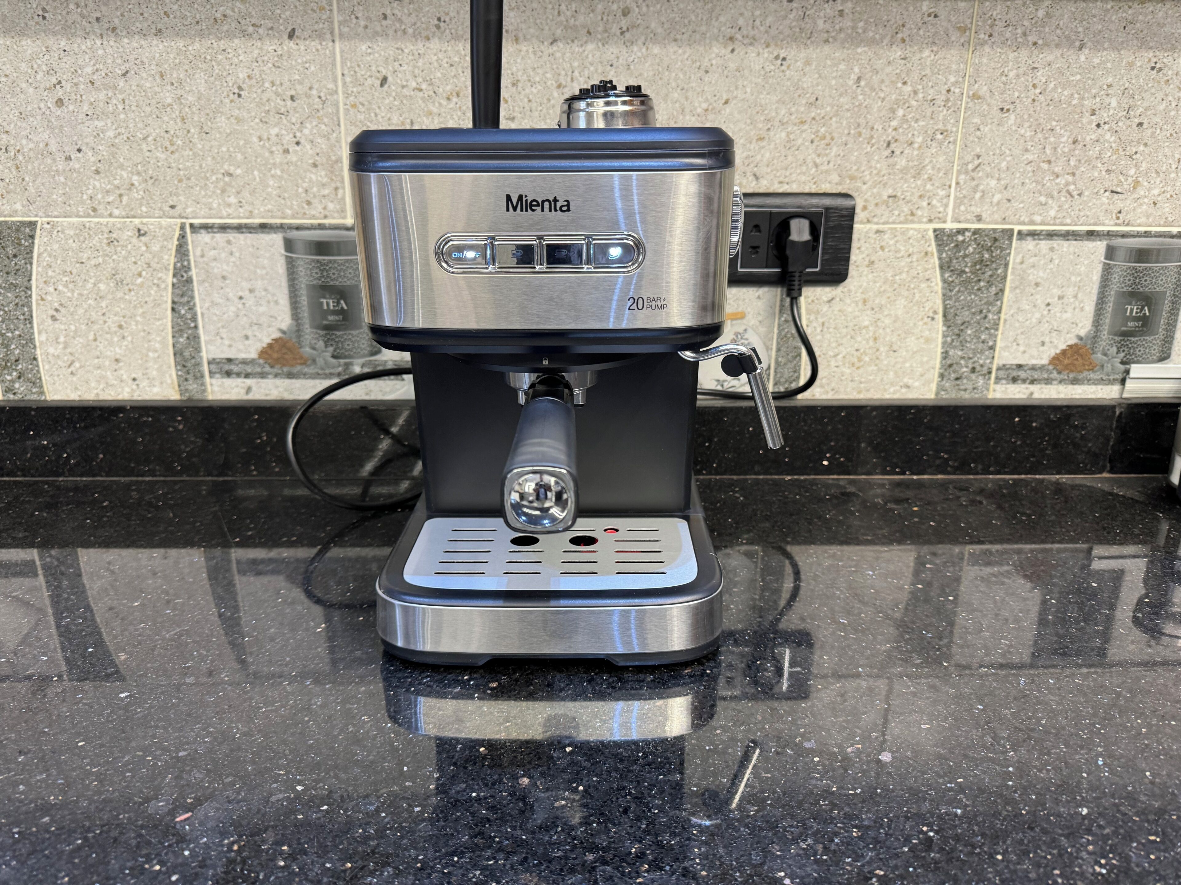 A Mienza coffee machine with a 20-bar pump, connected to a power outlet on a black countertop.