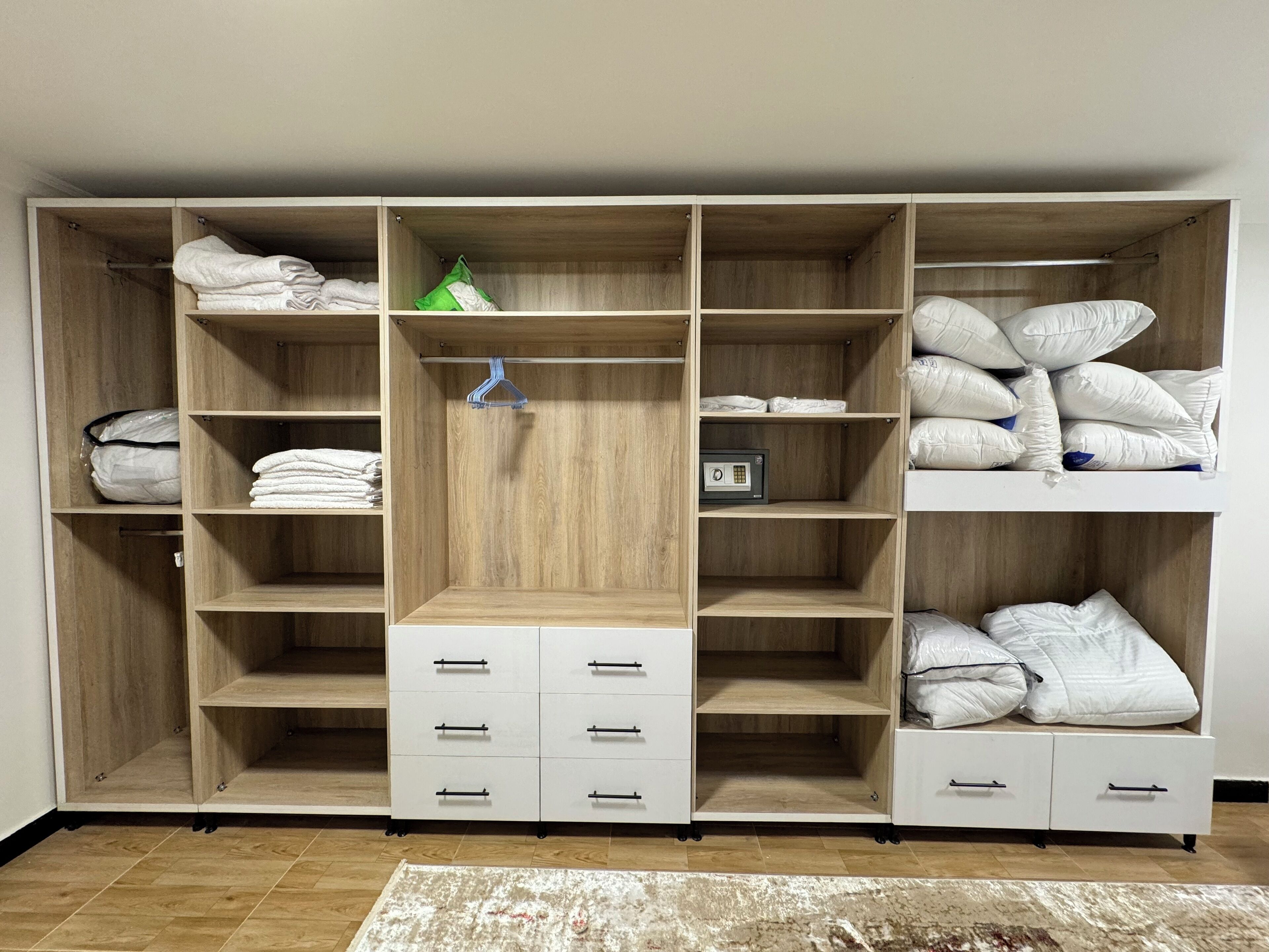 A spacious walk-in closet with multiple shelves, drawers, and hanging space, featuring neatly folded towels and neatly stacked pillows.