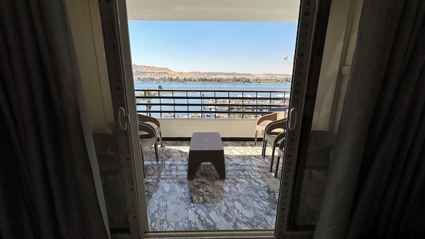 A room with a view of a lake and mountains, featuring a marble floor and a small table with chairs. - Relaxation (Aswan)