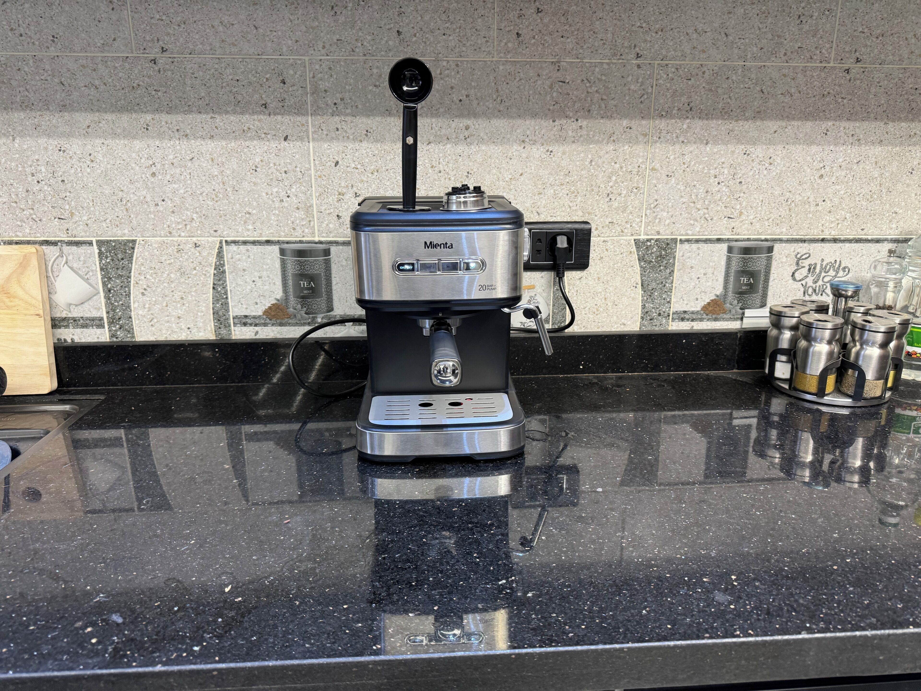 A coffee maker on a kitchen counter with a tiled backsplash and a sign that says "Enjoy Your Tea."