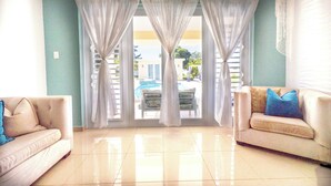 A living room with two sofas, a large window with white curtains, and a view of a swimming pool.