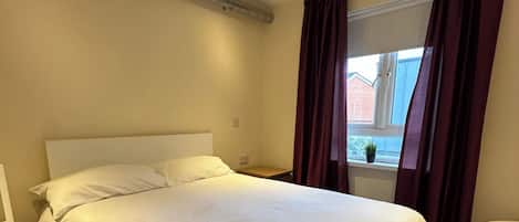 A hotel room with a large bed, a window with curtains, a bedside table, and a small table.