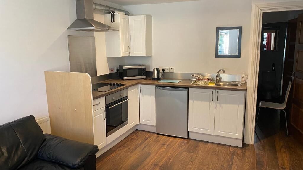 Cocina compacta con armarios blancos, microondas, hervidor y pileta.