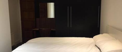 A bedroom with a bed, a dark wardrobe, a mirror, and a desk.