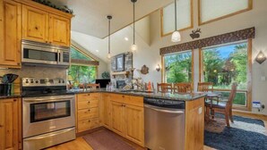 A modern kitchen with wooden cabinets, stainless steel appliances, and large windows offering a view of the outdoors. - Elk River Cabin – On Big Thompson River, Near RMNP, Estes Park – 23-ZONE3554 (Estes Park)