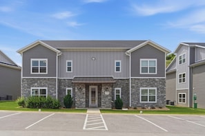A multi-story building with a stone facade, a central entrance, and a parking lot in front.