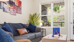 A living room with a grey sofa, a coffee table, a plant, and a window with a view of greenery.